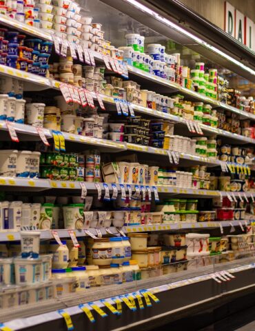 Aisle in a grocery store's refrigerated dairy section filled with yogurt cups and tubs on shelves.