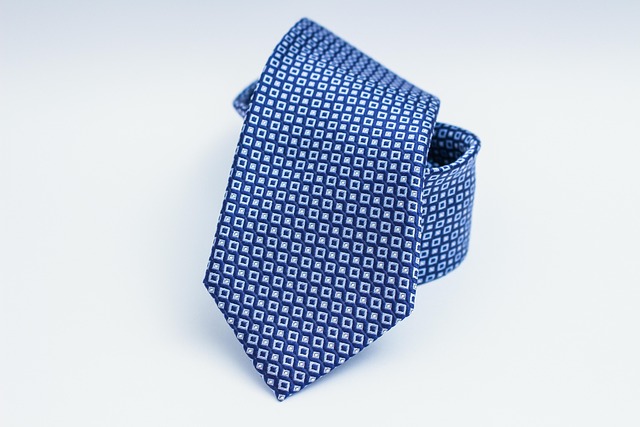 Blue necktie with a small white square geometric pattern, rolled at the knot for display.