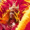 Carnival performer in a red-gold feather headdress with sequined crown, smiling at the camera.