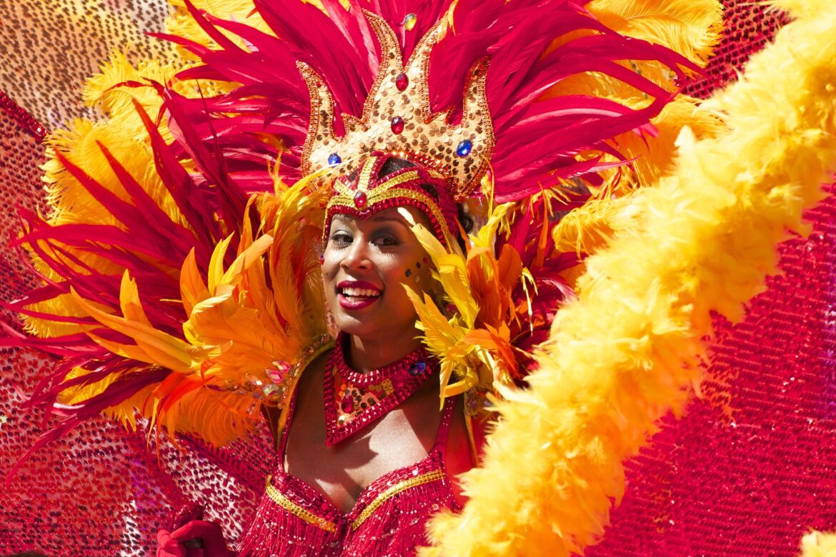 Carnival performer in a red-gold feather headdress with sequined crown, smiling at the camera.