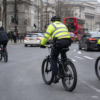 Two police officers on bicycles patrol a city street with a red double-decker bus in the background.",
