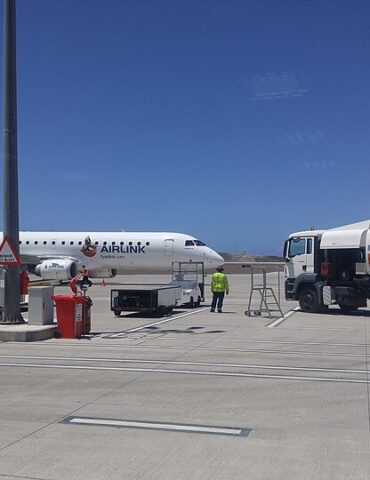 Airlink commuter jet on the tarmac with ground crew and a fuel truck nearby under a clear blue sky
