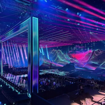 Futuristic nightclub stage with neon frames, purple-blue lasers, and a LED backdrop; crowd seated and watching a performance.