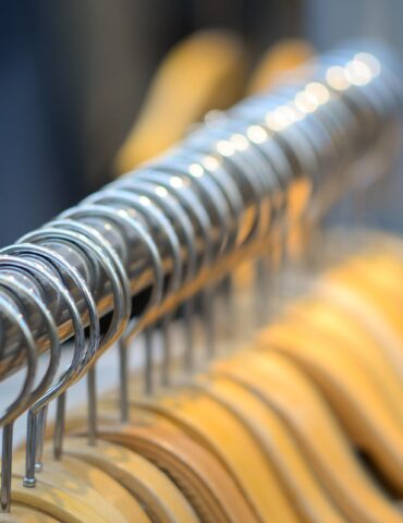 Close-up of metal spiral hangers on a clothes rack with wooden hangers blurred in the background.