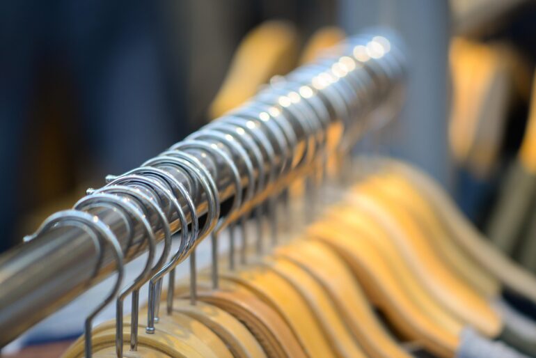 Close-up of metal spiral hangers on a clothes rack with wooden hangers blurred in the background.