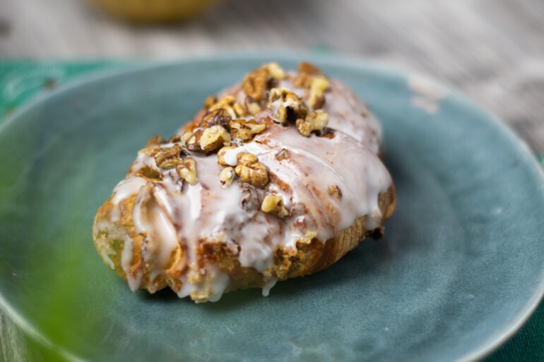 rogal - NOTE.radio - Polskie radio w UK | Polskie radio w Londynie Pastry with white icing and chopped walnuts on a blue-green plate, close-up shot.