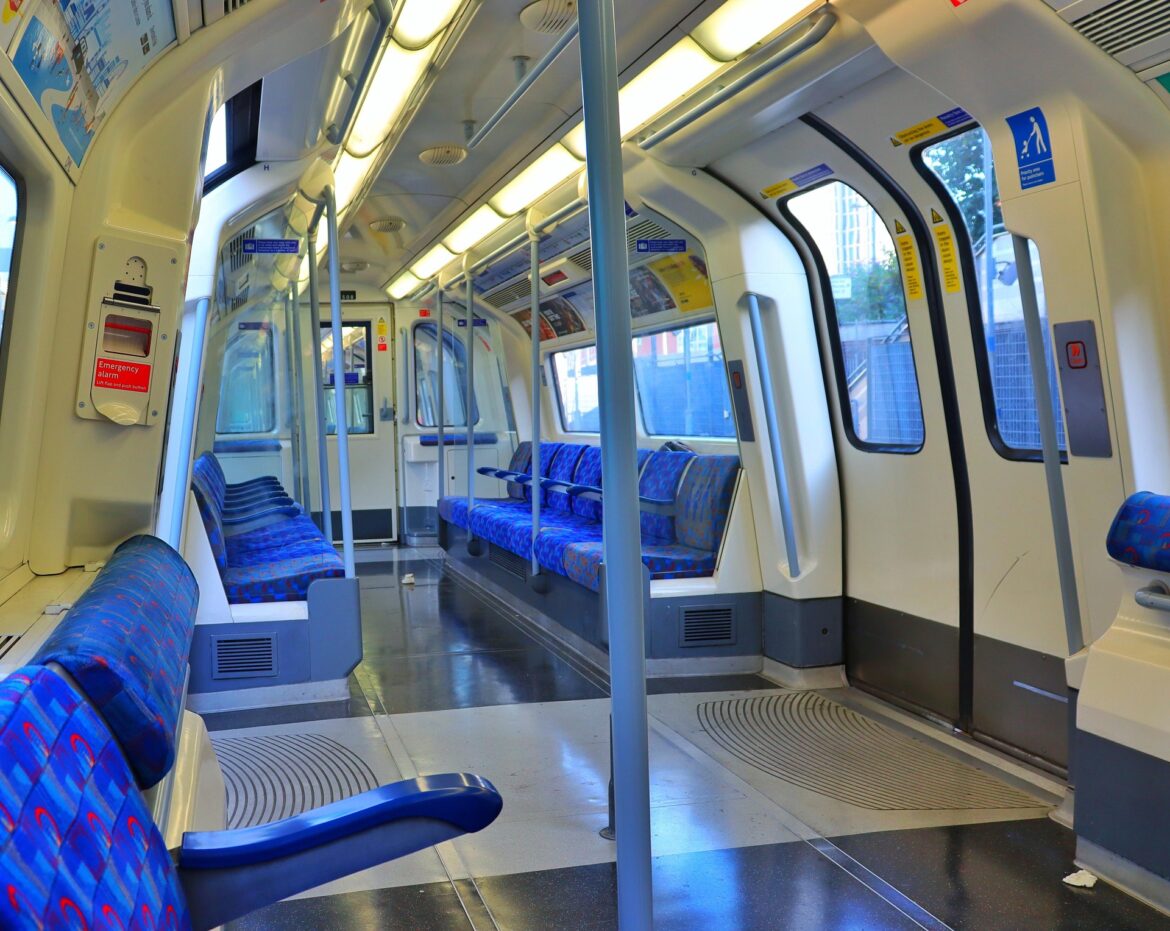 Inside a passenger train car with blue patterned seats along a narrow aisle and overhead lighting.
