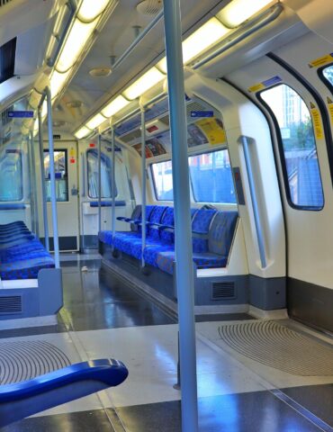 Inside a passenger train car with blue patterned seats along a narrow aisle and overhead lighting.