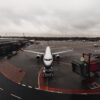 Passenger jet parked at the gate with a jet bridge to the right and an overcast sky above.