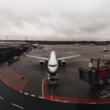 Passenger jet parked at the gate with a jet bridge to the right and an overcast sky above.