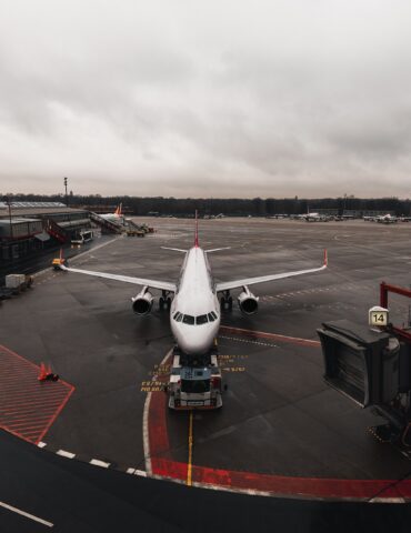 Passenger jet parked at the gate with a jet bridge to the right and an overcast sky above.