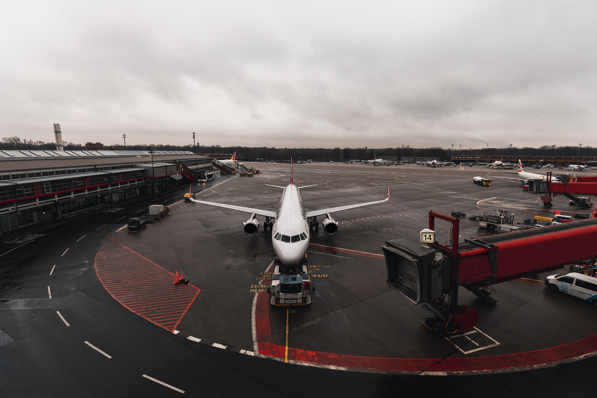 Passenger jet parked at the gate with a jet bridge to the right and an overcast sky above.