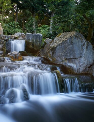 Gentle multi-tiered waterfall flowing over rocks in a lush garden setting