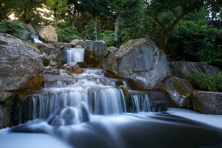 Holland park - NOTE.radio - Polskie radio w UK | Polskie radio w Londynie Gentle multi-tiered waterfall flowing over rocks in a lush garden setting