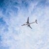White passenger airplane flying high in a blue sky with wispy clouds.