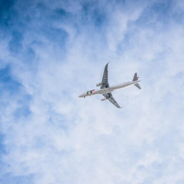 White passenger airplane flying high in a blue sky with wispy clouds.