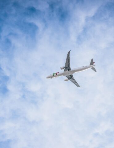 White passenger airplane flying high in a blue sky with wispy clouds.