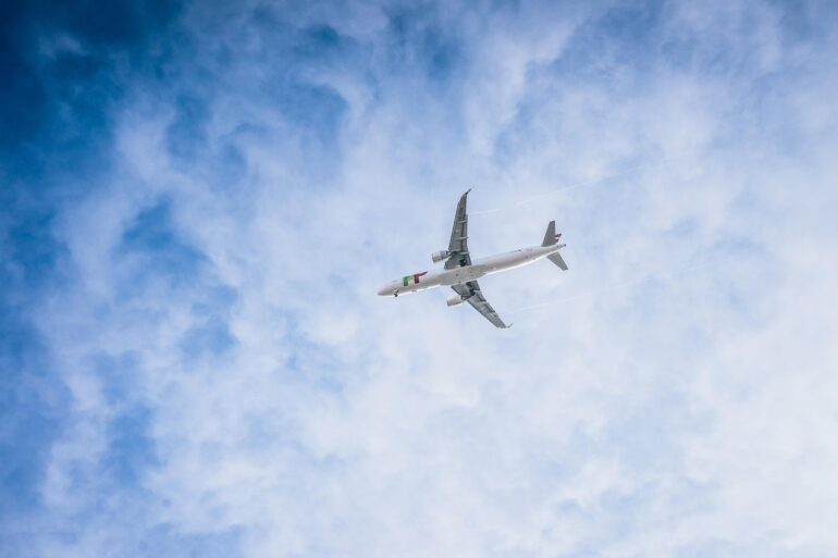 White passenger airplane flying high in a blue sky with wispy clouds.