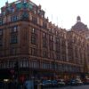 Harrods department store façade lit with festive string lights on a busy London street at dusk.