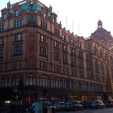 Harrods department store façade lit with festive string lights on a busy London street at dusk.