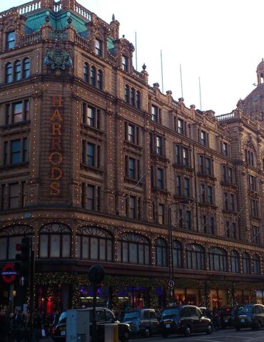 Harrods department store façade lit with festive string lights on a busy London street at dusk.
