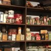 Shelf of vintage metal tins and small glass bottles on dark wooden shelving, resembling an antique shop display with folded items on top.