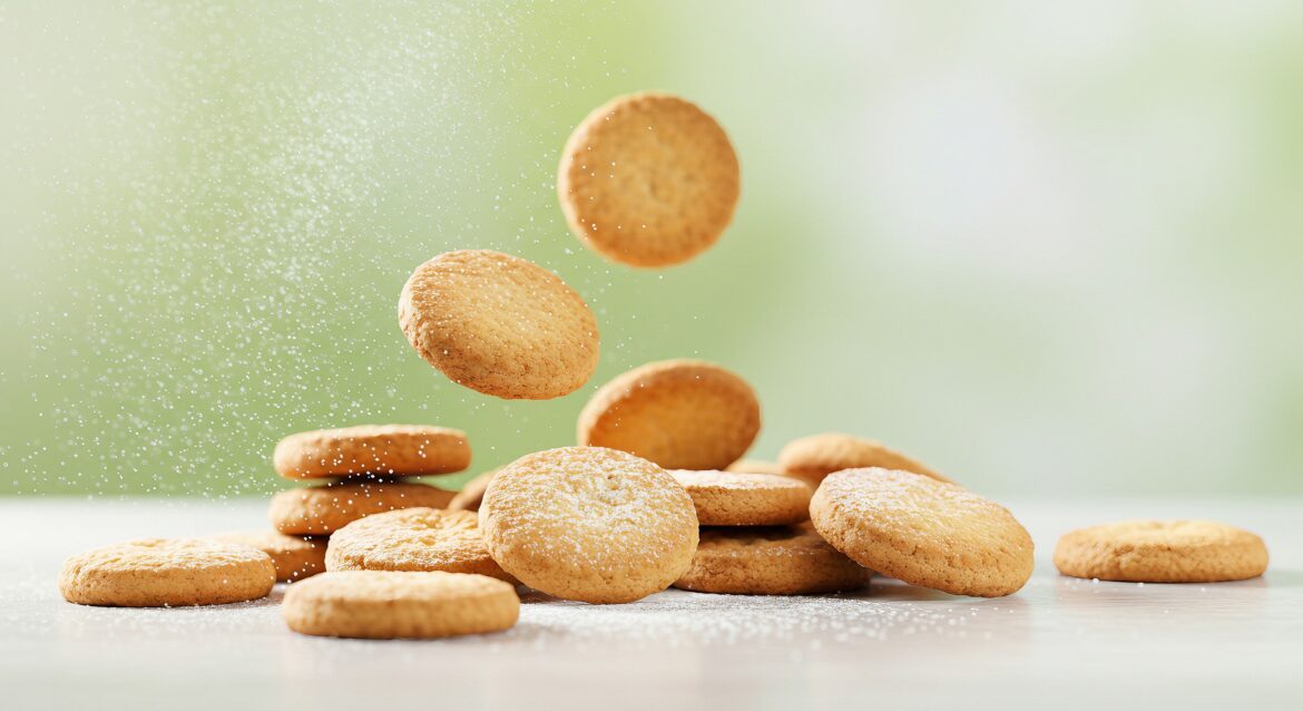 Golden round cookies piled and scattered on a white surface, fine sugar dust floating in the air.