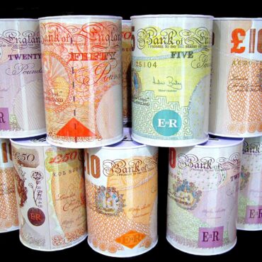 Rolled Bank of England banknotes in different denominations (£10, £20, £50) arranged in vertical stacks against a dark background.