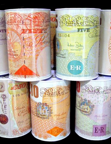 Rolled Bank of England banknotes in different denominations (£10, £20, £50) arranged in vertical stacks against a dark background.