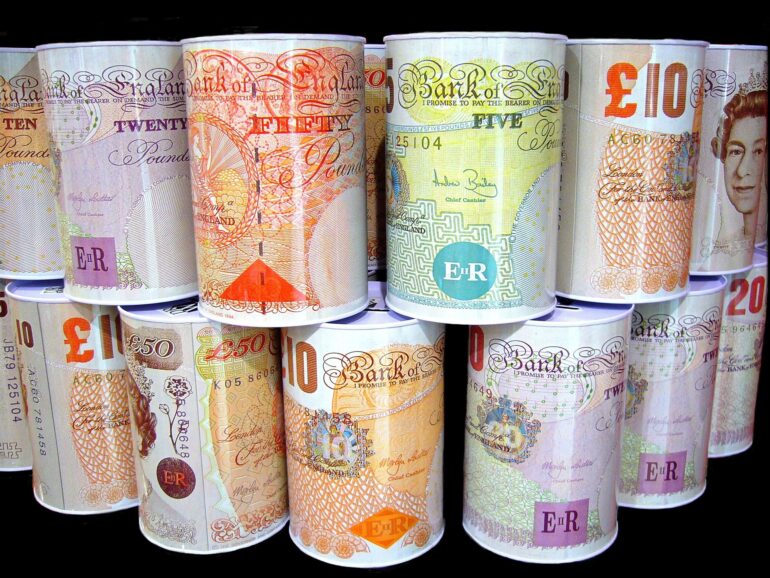 Rolled Bank of England banknotes in different denominations (£10, £20, £50) arranged in vertical stacks against a dark background.