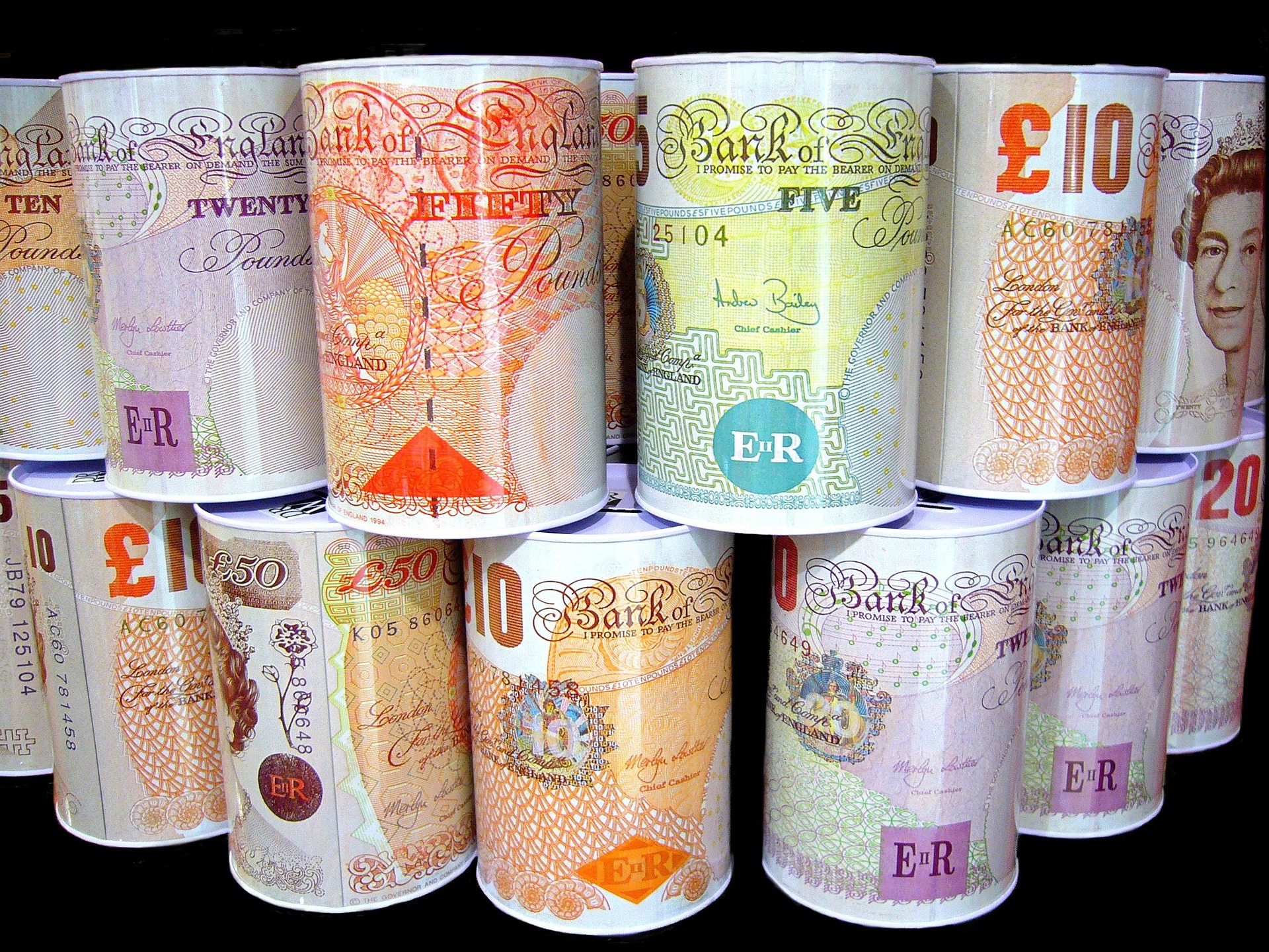 Rolled Bank of England banknotes in different denominations (£10, £20, £50) arranged in vertical stacks against a dark background.
