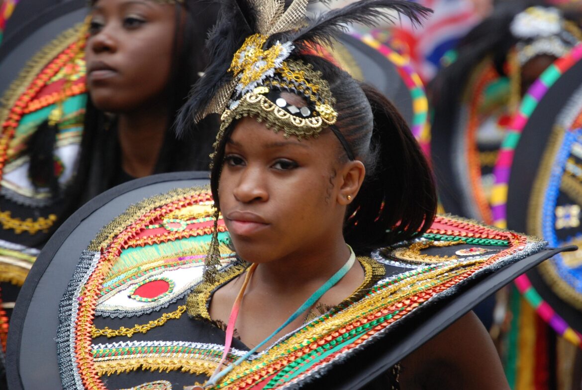 Young woman in a colorful carnival costume with gold beadwork, feathers, and a large decorative shield hold.