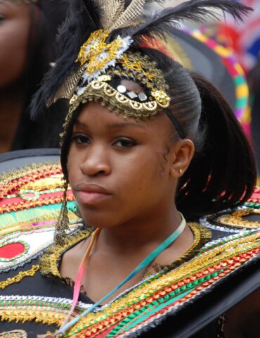 Young woman in a colorful carnival costume with gold beadwork, feathers, and a large decorative shield hold.
