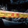 Yellow caution tape reading 'Warning Restricted Access' stretched across burned rubble, blocking a damaged building.