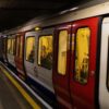 A London Underground train stopped at an underground platform, with passengers inside and a few people waiting on the platform edge.