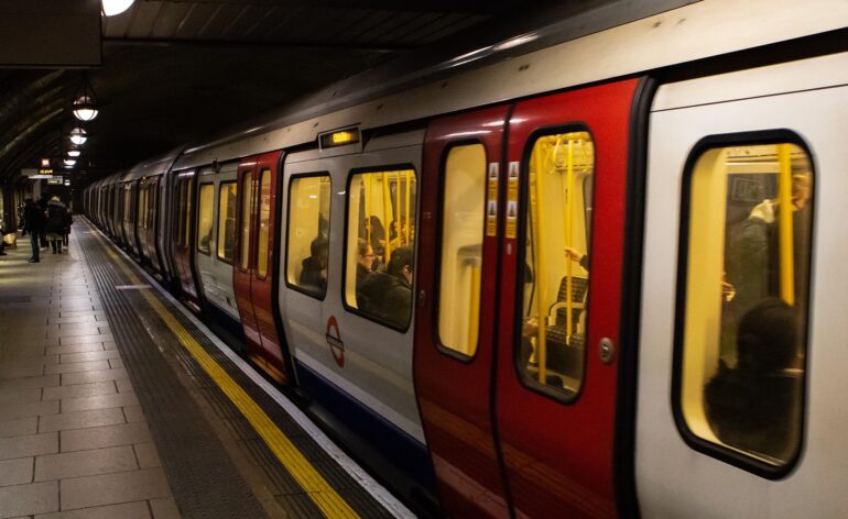 METRO - NOTE.radio - Polskie radio w UK | Polskie radio w Londynie A London Underground train stopped at an underground platform, with passengers inside and a few people waiting on the platform edge.