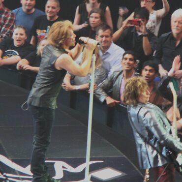 Rock singers perform on stage with fans in the front row reaching out and taking photos beyond them