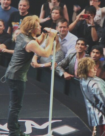 Rock singers perform on stage with fans in the front row reaching out and taking photos beyond them