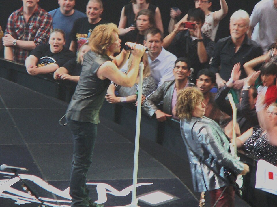 Rock singers perform on stage with fans in the front row reaching out and taking photos beyond them