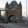 Brick gateway over a roadway leading to a tunnel, with height clearance signs above the lane and striped supports on either side.