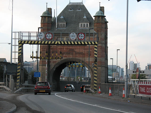 Brick gateway over a roadway leading to a tunnel, with height clearance signs above the lane and striped supports on either side.