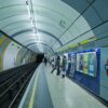 London Underground Bond Street platform with passengers waiting beside ads and curved ceiling panels.