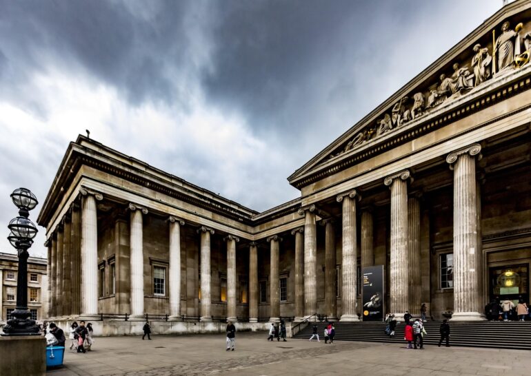 hulkiokantabak-british-museum-5200528_1920 - NOTE.radio - Polskie radio w UK | Polskie radio w Londynie Grand neoclassical building with tall columns and a sculpted pediment, people walking in the square under a cloudy sky.