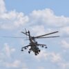 Military helicopter in flight with spinning rotor blades against a blue sky with clouds.