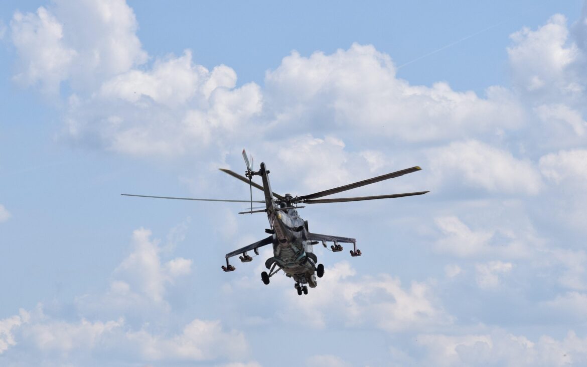 Military helicopter in flight with spinning rotor blades against a blue sky with clouds.