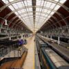 Inside a large train station with a curved glass and steel roof and trains at the platforms beneath it
