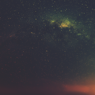 Colorful night sky filled with many stars and a soft aurora glow across the horizon in oranges, greens, and yellows.