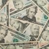 Overlapping U.S. dollar bills (various denominations) scattered in a collage scene, showing portraits and security features.