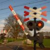 Railroad crossing with lowered barriers, red flashing lights, and tracks in the foreground in a rural setting
