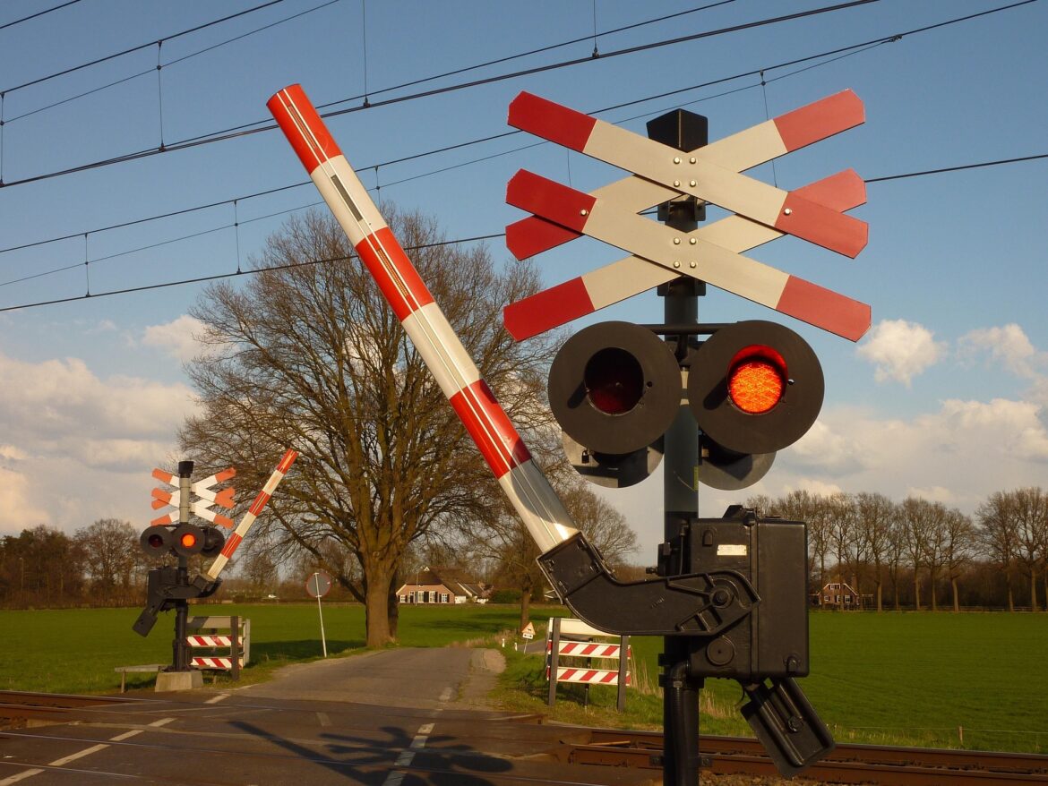 Railroad crossing with lowered barriers, red flashing lights, and tracks in the foreground in a rural setting